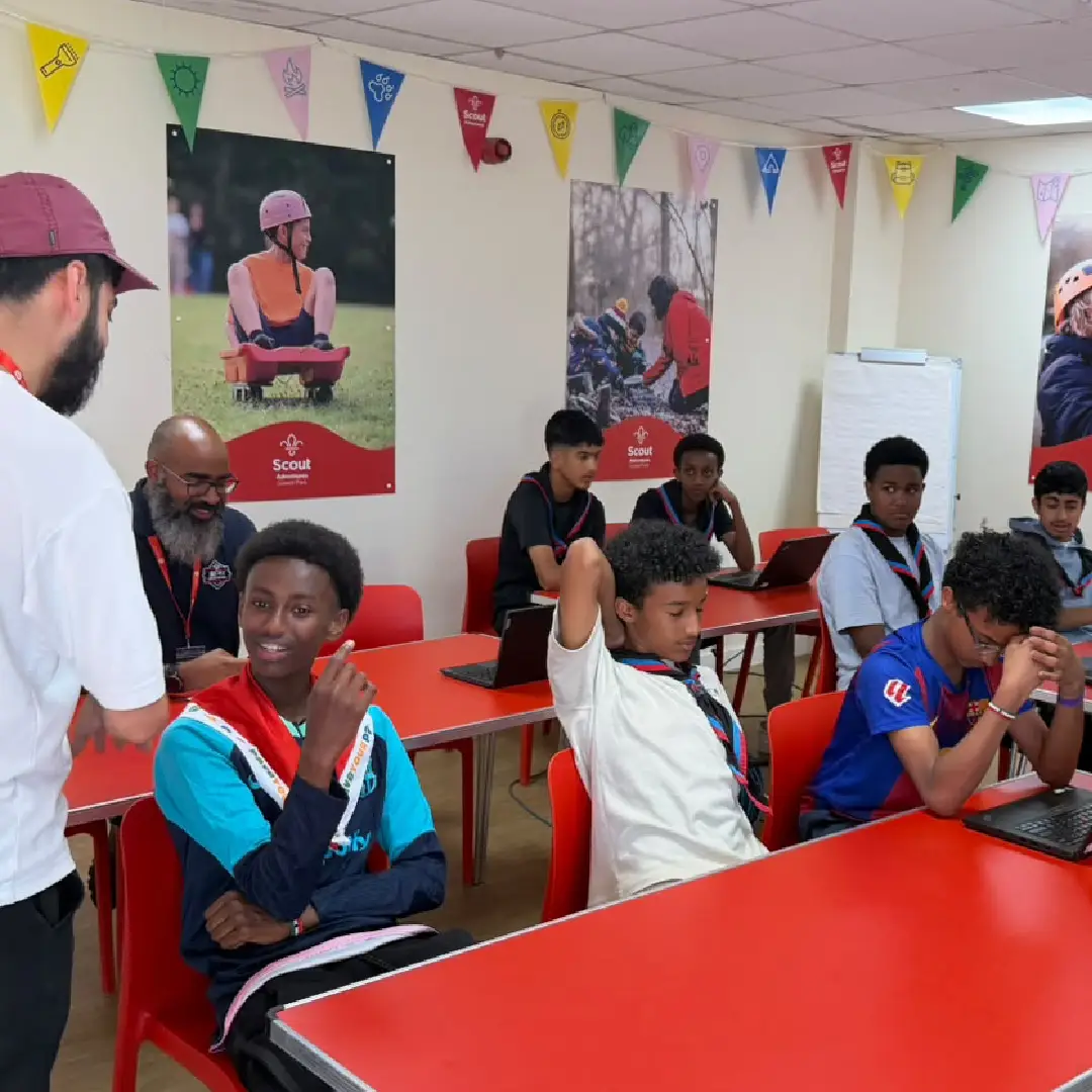 Scouts and volunteers gathered around laptops during a workshop